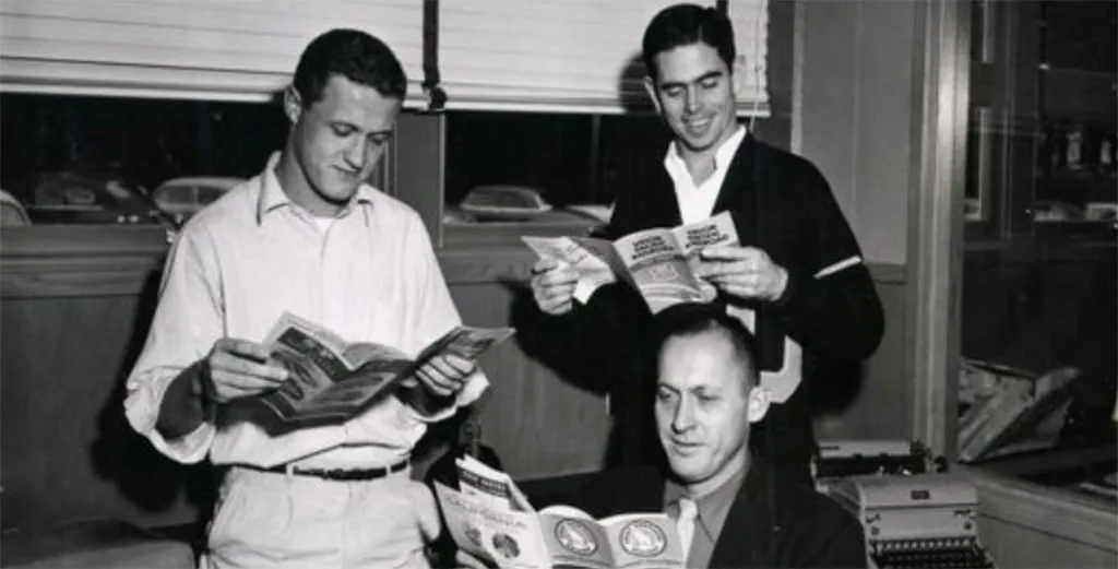 Bill Dellinger, Jim Bailey, and Bill Bowerman pose reading pamphlets.