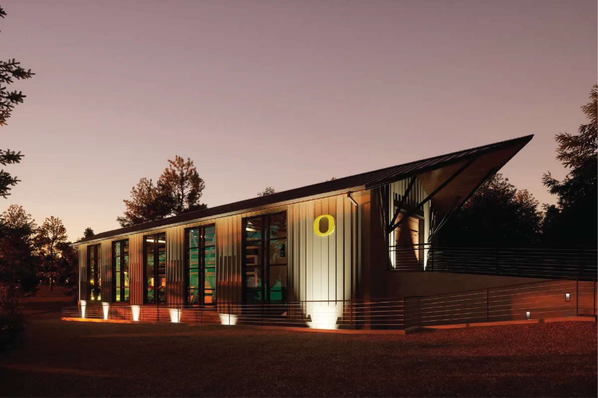 The UO Boathouse with lights illuminating the walls at night. 