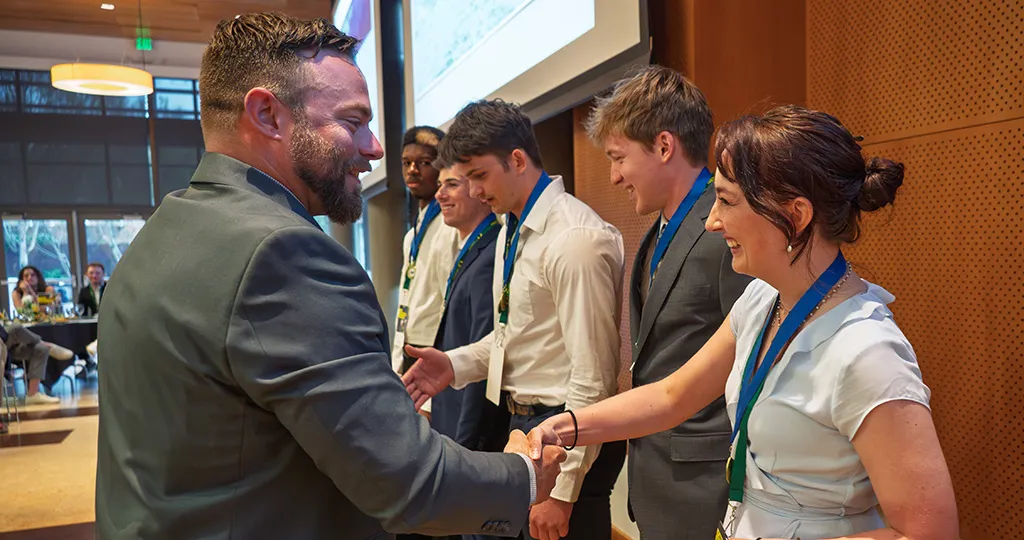 Oregon Rowing Head Coach Josh Baker shakes hands with rowers during the 2025 Spring Fundraising Dinner.
