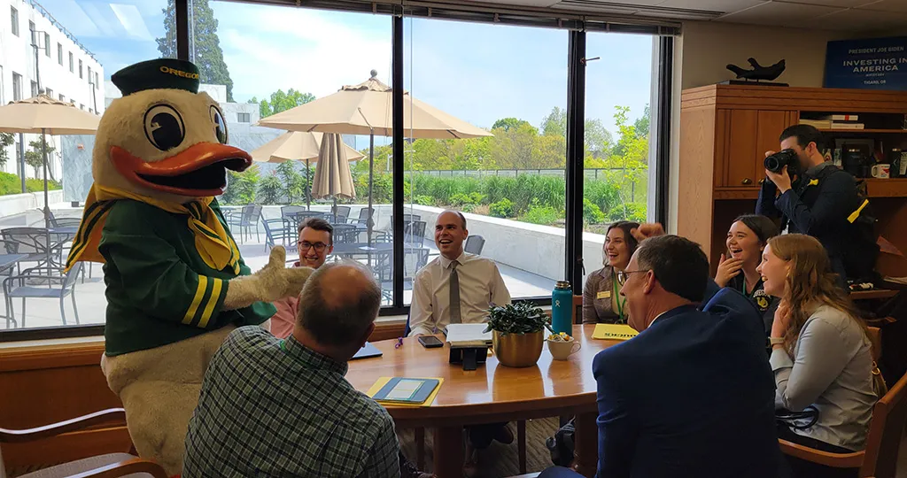 The Duck mascot standing next to a table full of people sitting while laughing and engaging. 