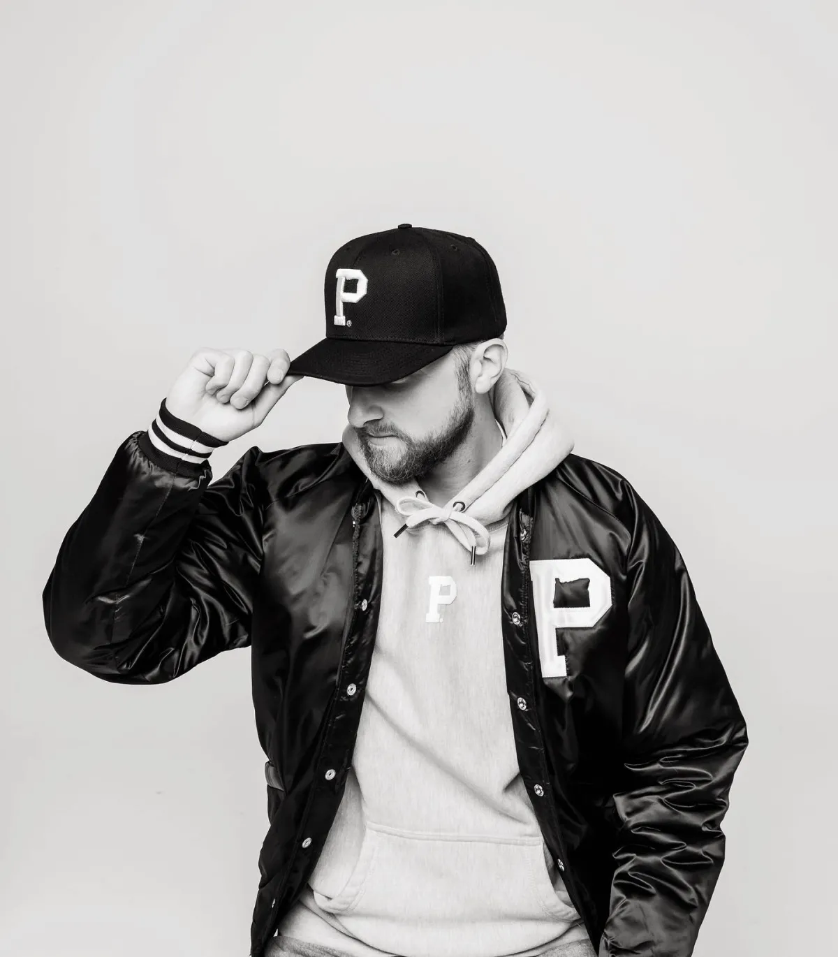 Person in branded 'P' hoodie, varsity jacket, and cap posing against a plain background.