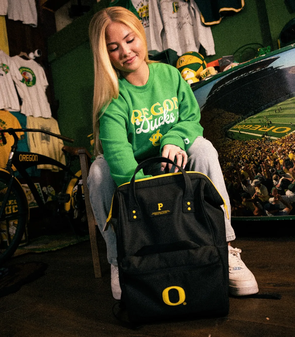 Person in Oregon Ducks gear holding a branded backpack inside a fan merchandise store.