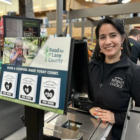 A woman standing behind a cash register with Food for Lane County flyers attached. 