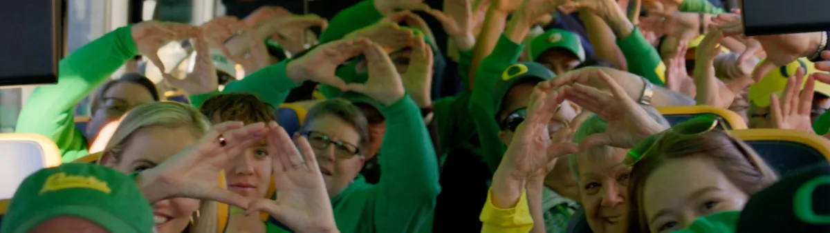 A bus full of Ducks fans wearing green make Os with their hands, holding them above their heads and into the aisle.