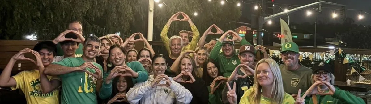 A group of Ducks fans pose on an outside patio at a watch party, smiling at the camera and making Os with their hands.