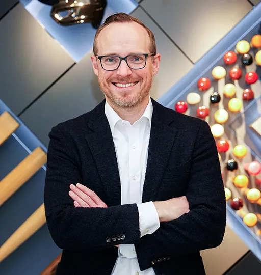 A person smiling while crossing their arms in front of a modern decorated wall. 