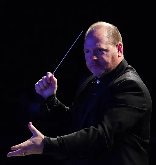 A music conductor demonstrating hand motions while in a dark room. 
