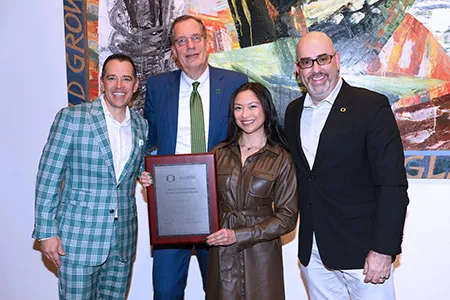 Lorie Acio holds the Distinguished Young Alumni award among UOAA Executive Director Raphe Beck, University of Oregon President Karl Scholz, and UOAA Board of Directors President Anthony Lambatos.