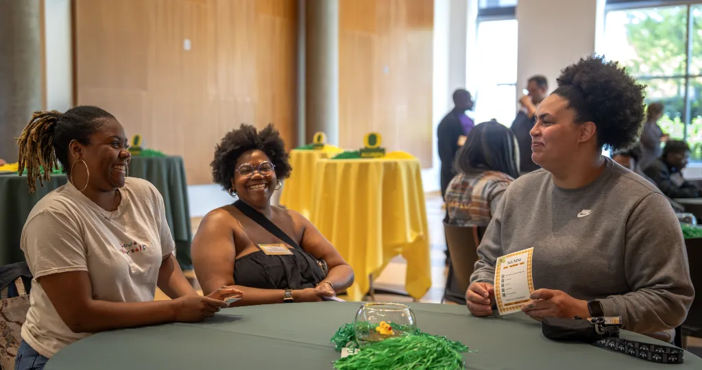Three Black UO alumni sit around a table together talking.