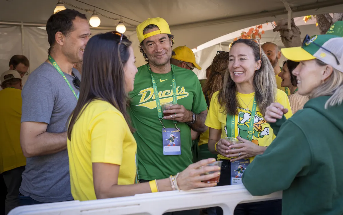 UO alumni in green and yellow smile together in a tailgate tent.