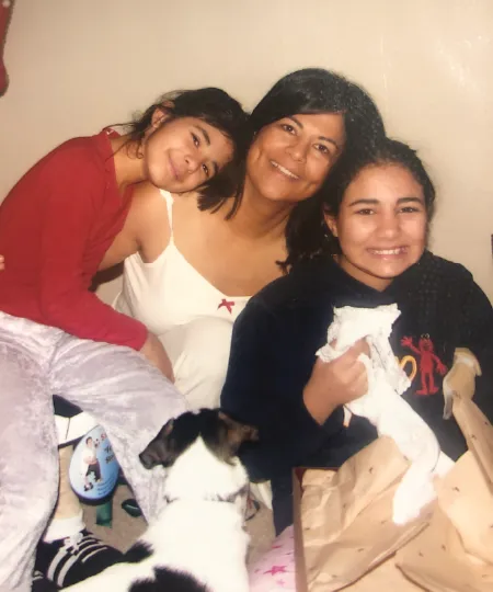 A mother sitting, holding her two daughters on each side all smiling. 