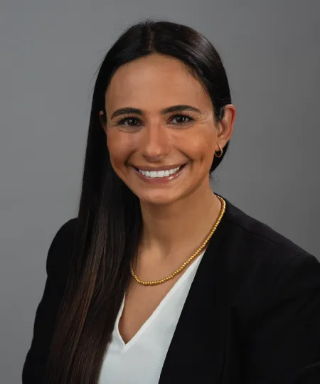 A headshot of a woman in a black blazert and grey background. 