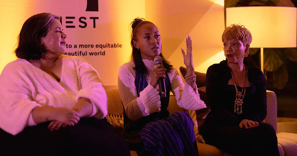 Nia peaks into a microphone while sitting between two women on a couch.