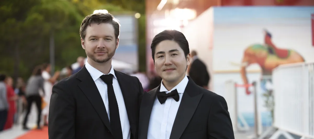 Two adult males standing together wearing tuxedos. 