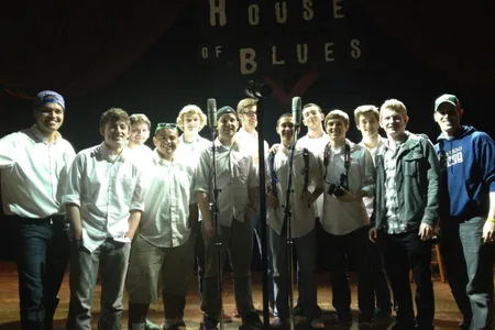 The members of On the Rocks wear white shirts on a dark stage with the words House of Blues behind them