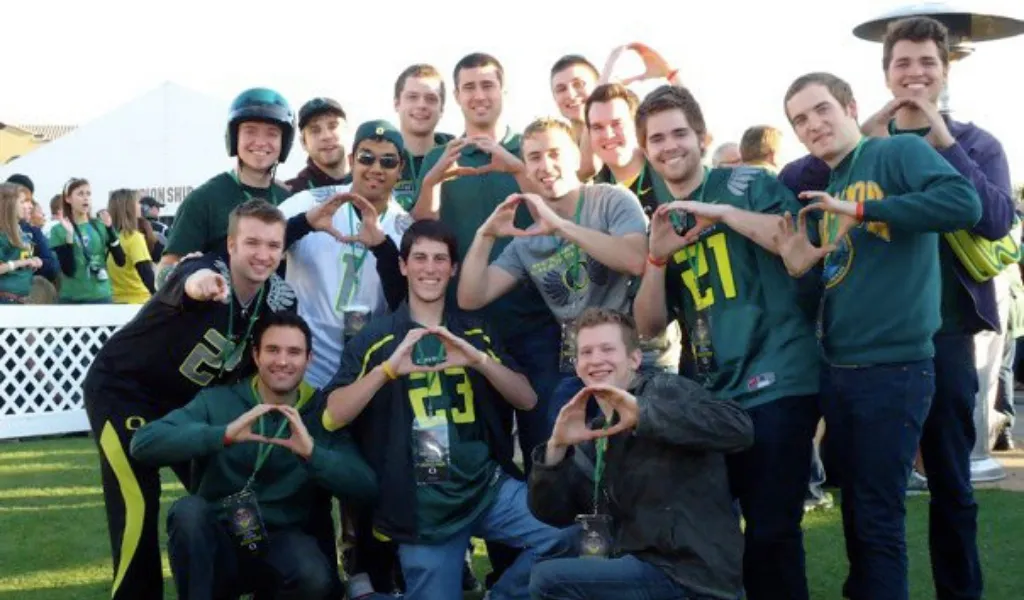 The 2010 members of On the Rocks make the shape of an O with their hands at a tailgate event. They are all wearing University of Oregon shirts including jerseys for the football team.