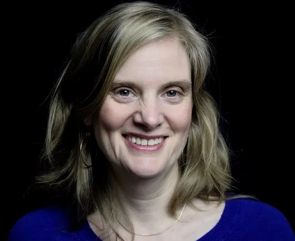 A headshot of Aubrie De Clerck, a blonde white woman in a blue shirt on a black background.