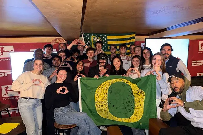 UO alumni hold an Oregon flag at a football watch party