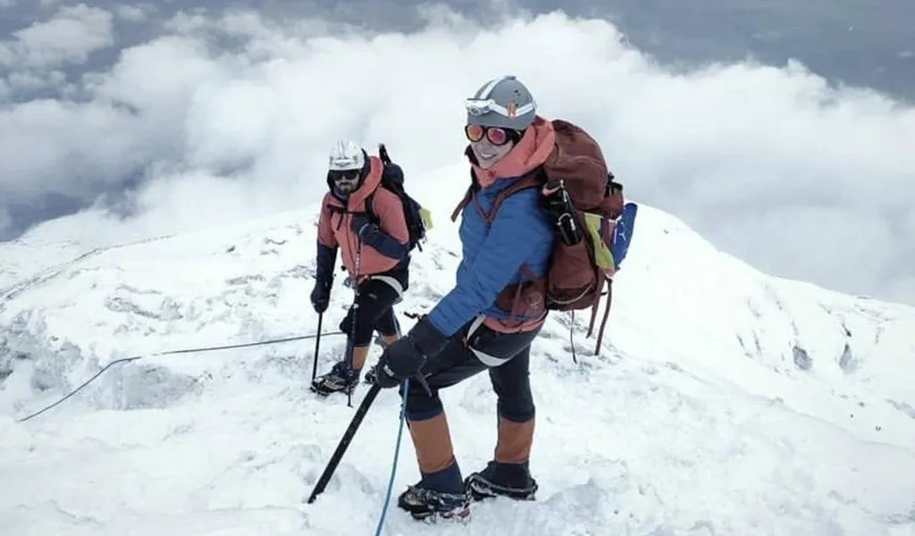 Ben Clark and Sabrina Dake in climbing gear on the snowy side of a mountain looking up at a camera.