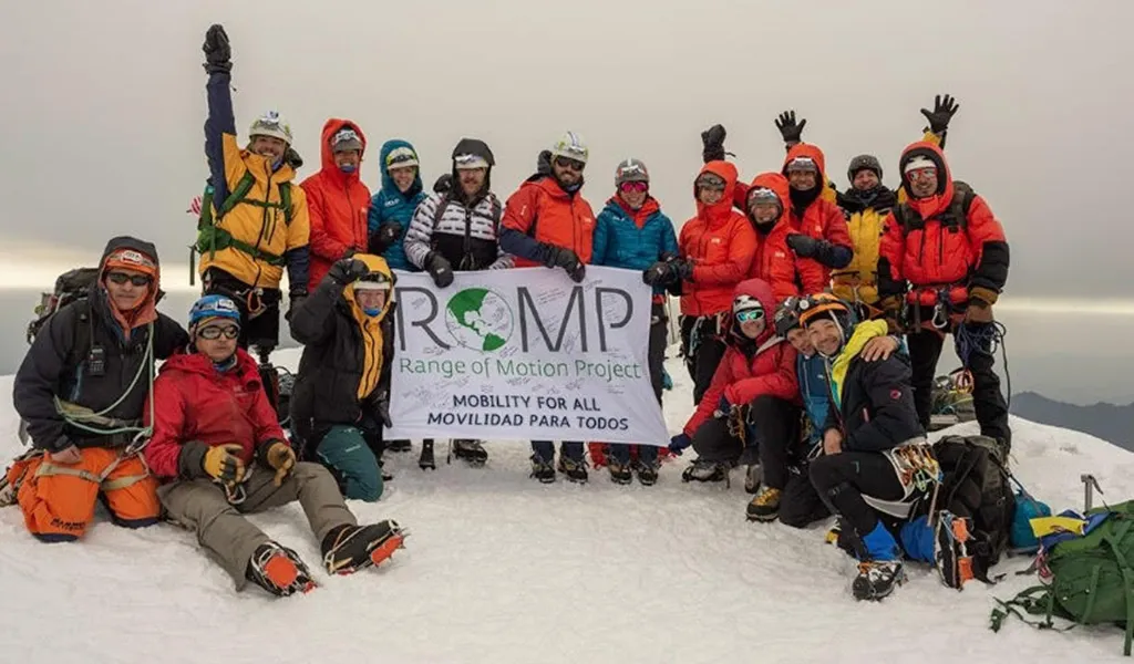 A group of people in climbing gear hold a banner that says ROMP at the summit of Mount Cotopaxi in Ecuador.