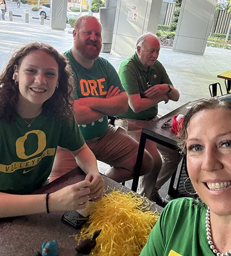 Two men, a woman, and a young girl in Oregon Ducks merch smile in a selfie.