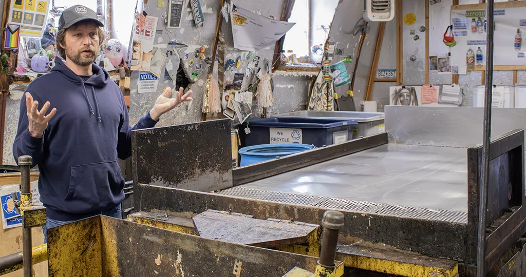 A man in a blue hoodie stands next to a metal table with metal sheets on the sides.