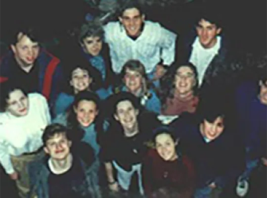 A group of students in the early 1990s smiling up at a camera as group.