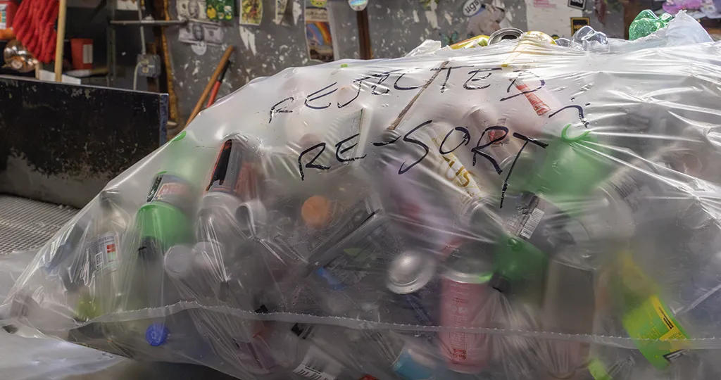A clear plastic bag filled with cans and bottles labeled with Sharpie that says "Rejected Re-sort" with a sad face.
