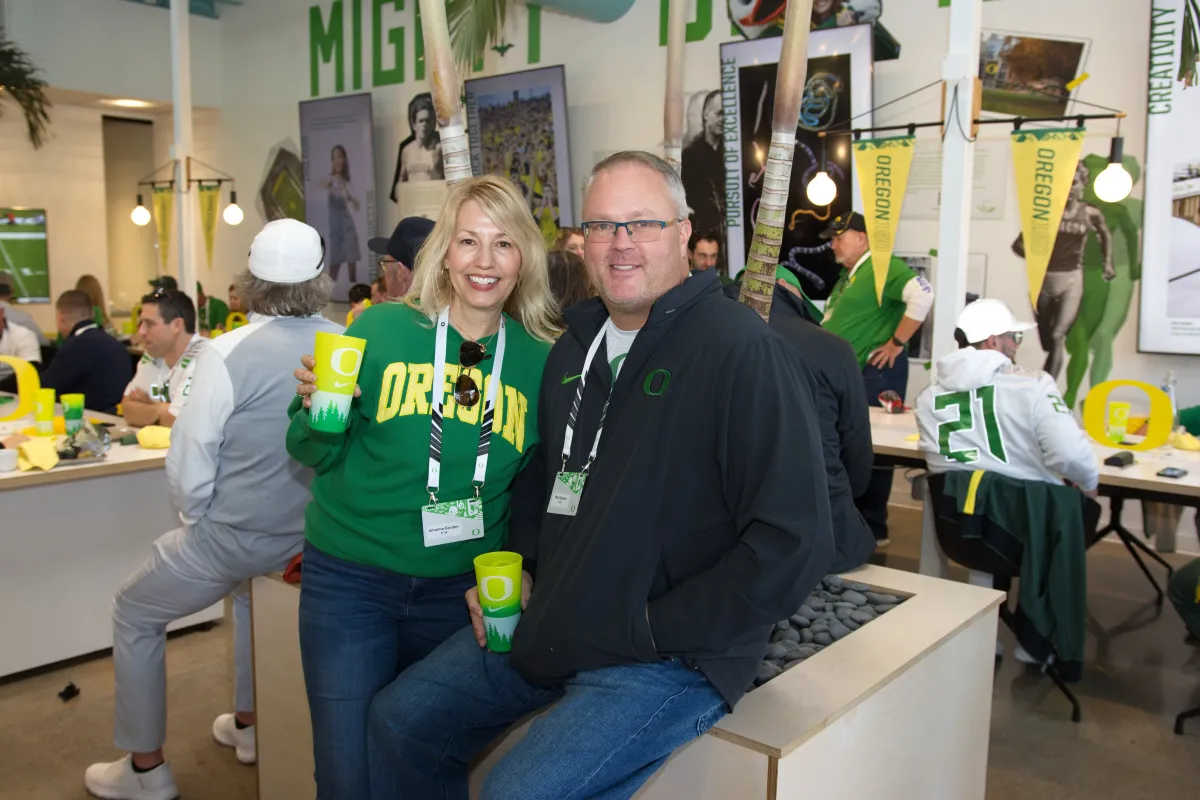 A man and a woman in Oregon Ducks gear smile at the camera, surrounded by Oregon decorations.