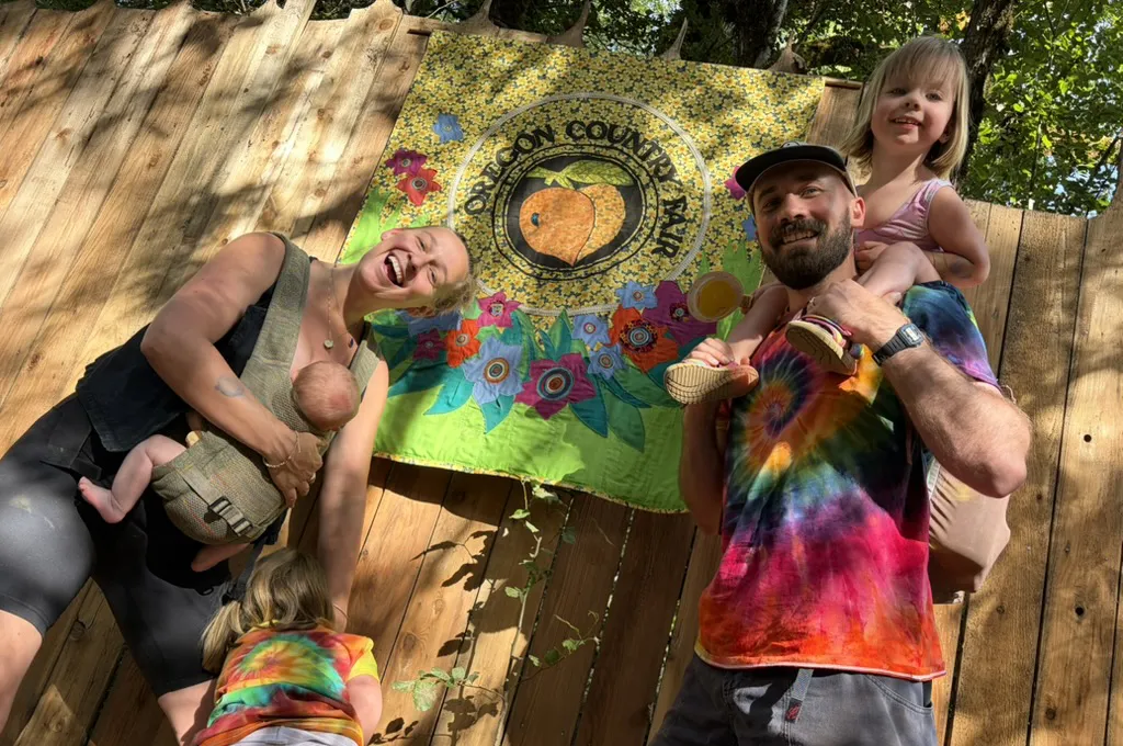 The Flannerys smile in multi-colored clothes in front of a sign that says Oregon Country Fair.