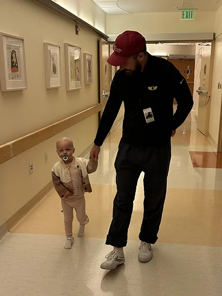 Kevin Flannery holds Shea's hand as they walk down a hospital hallway.