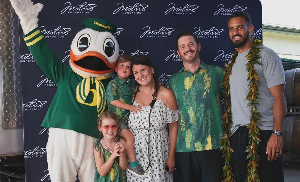 Marcus Mariota stands with a family and the Oregon Duck in front of a photo station for the Motiv8 Foundation.