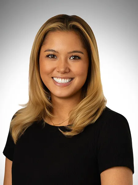 Alyssa Castro, a woman in a black shirt smiles on a gray background.