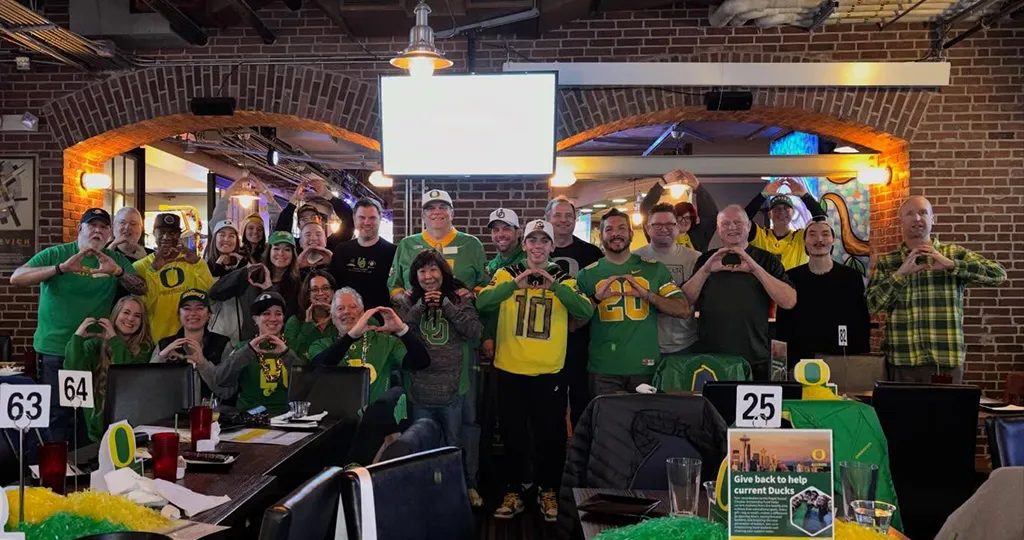 A large group of Seattle Ducks in Oregon gear pose for a photo at GameWorks, their venue.