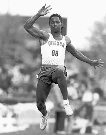 JJ Birden, a Black man, jumping in a black and white for in a University of Oregon track uniform.