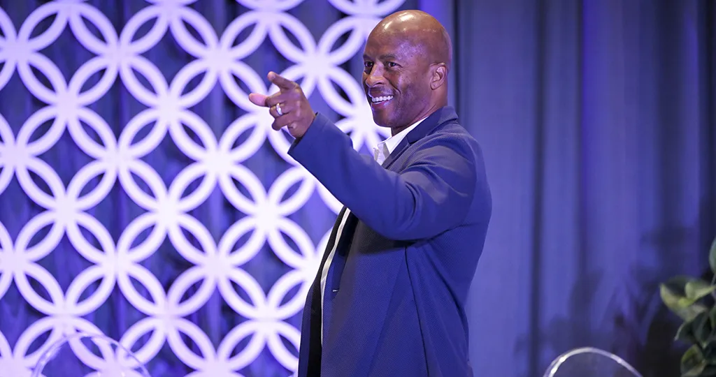 JJ Birden points his finger off stage, smiling in a suit.