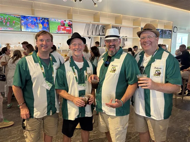 Four men in matching green and white shirts with the Duck embroidered below a nickname on the front smile together.