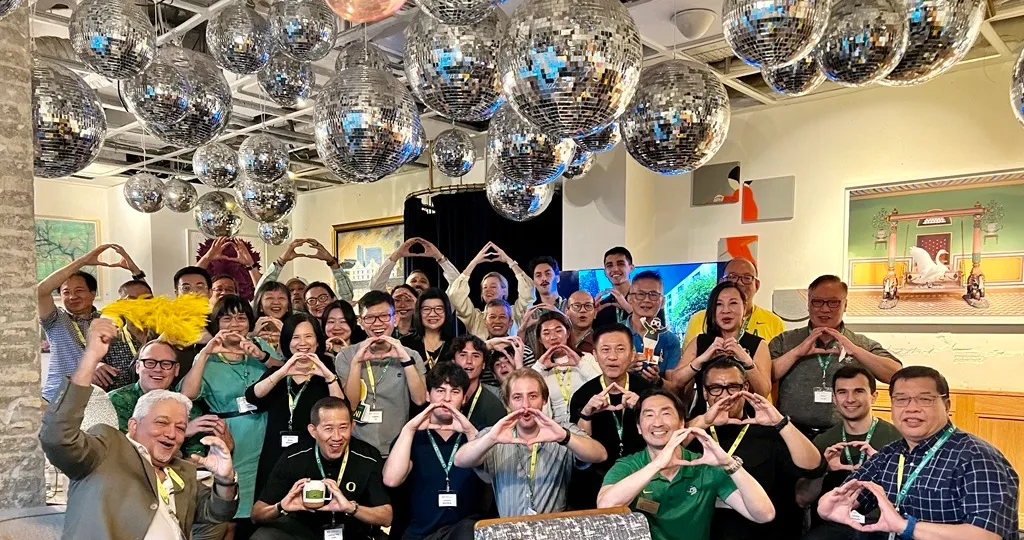 A group of people in Singapore standing under many hanging disco balls each make the shape of an O with their hands.