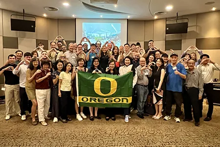 A large group of people gather around a green flag that says Oregon with the yellow Oregon "O" in the center.