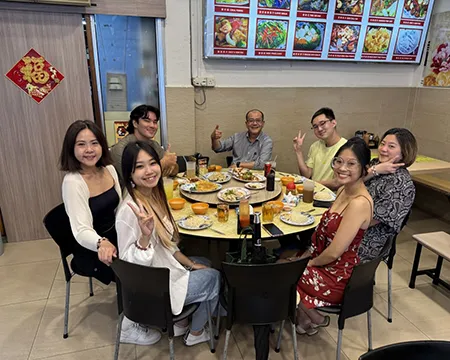 Seven people gather around a circle dining table in a restaurant serving Chinese food in Singapore.